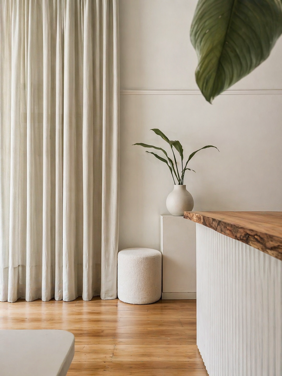 Detail of the live-edge timber reception counter with sheer curtain, white plinth, ceramic vase and boucle ottoman